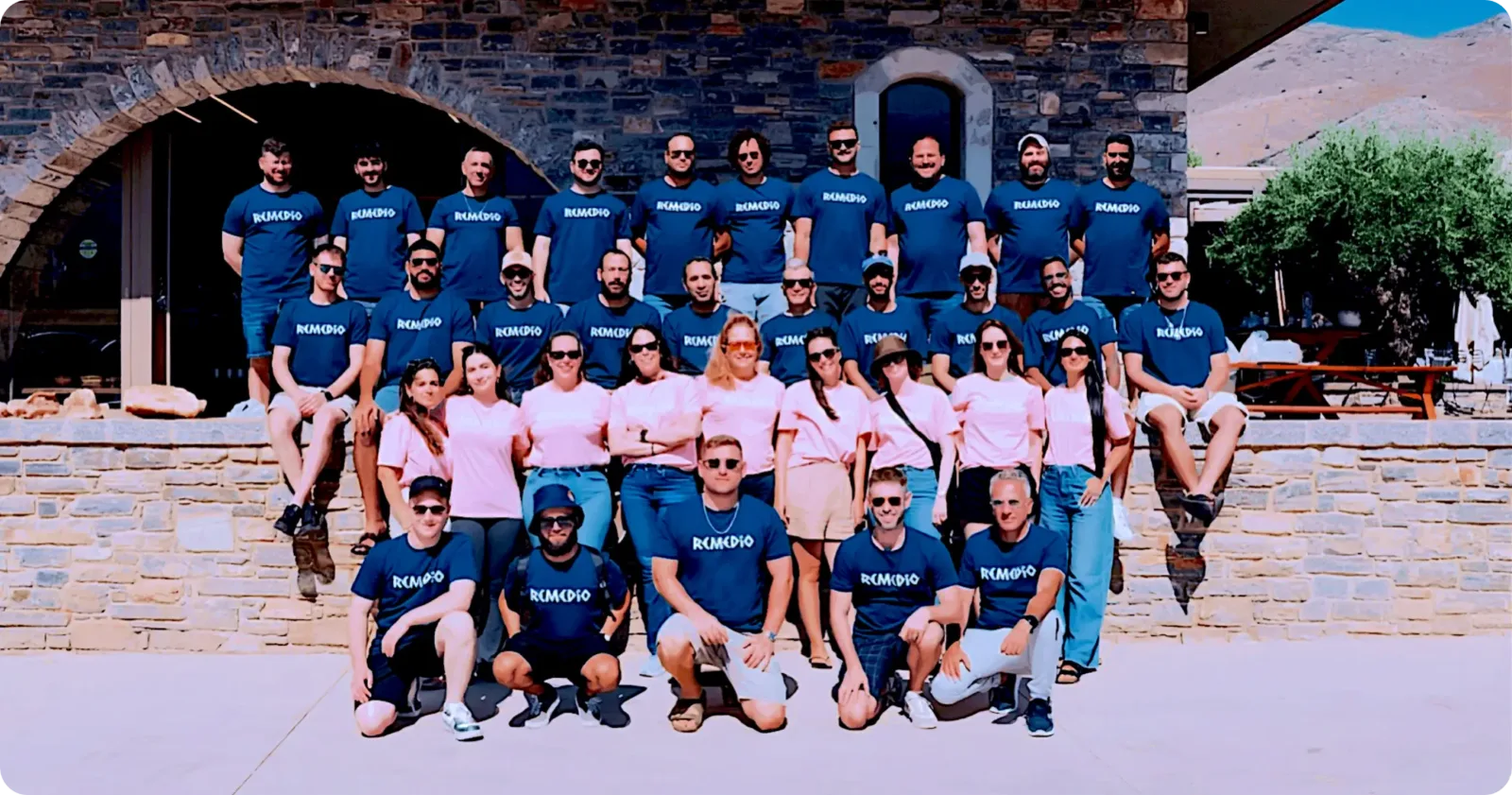 A group of people wearing matching blue and pink shirts pose for a group photo outside in front of a stone building.